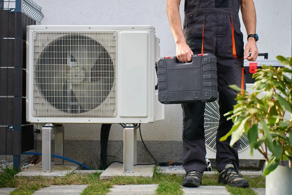 Un technicien GEOSOL en tenue professionnelle expliquant le fonctionnement d'une pompe à chaleur air/eau à un couple de propriétaires dans leur maison. Le technicien montre de la documentation technique ou pointe du doigt vers l'unité extérieure visible. L'atmosphère doit transmettre la confiance, le professionnalisme et l'accompagnement personnalisé. La scène se déroule en Lorraine, devant une maison résidentielle typique avec la PAC visible à l'arrière-plan.