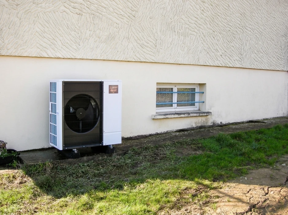Unité extérieure de pompe à chaleur air/air installée contre un mur de façade blanc, posée sur plots anti-vibratoires en caoutchouc sur dalle béton